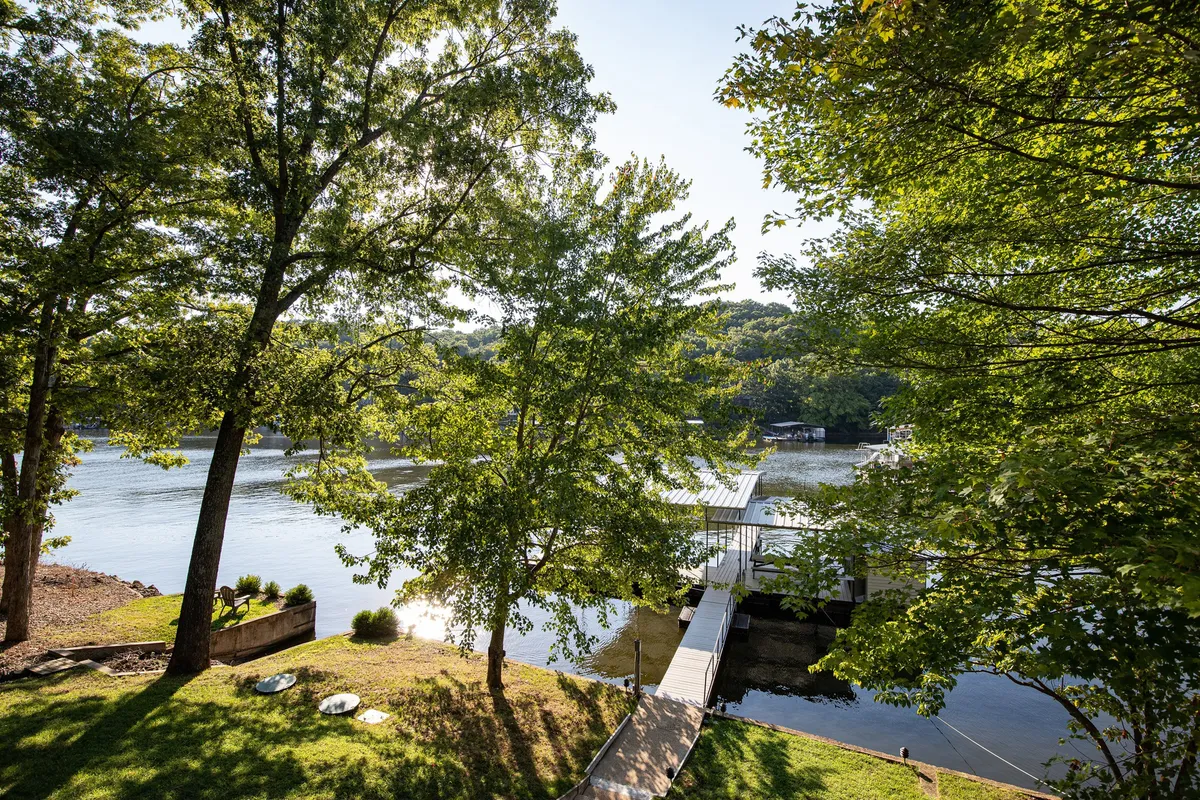 A tranquil dock stretches out into calm lake waters, surrounded by lush greenery. The gentle ripples on the water and the natural setting evoke a sense of peace and seclusion. The scene suggests opportunities for boating, fishing, or simply relaxing by the water's edge, with the soft lighting hinting at either a serene morning or a golden sunset.