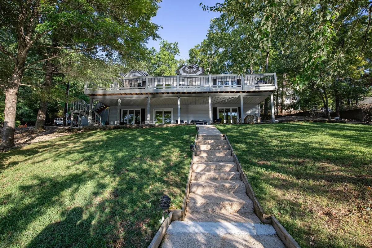 A welcoming house features a spacious deck overlooking a landscaped yard and a stone pathway leading through lush garden areas. The outdoor space is ideal for relaxing, socializing, and enjoying meals with a view of the surrounding nature.