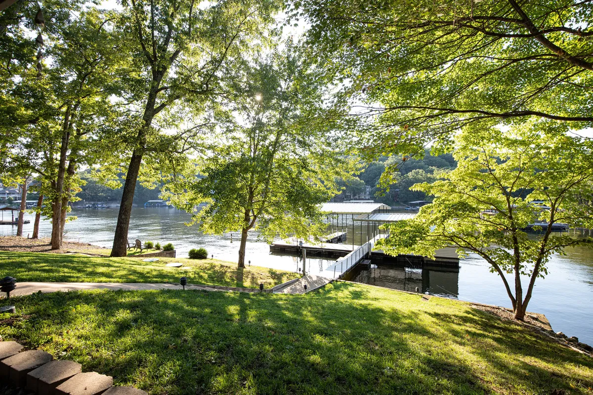 A peaceful scene with a dock extending over serene water, bordered by lush green trees and a boathouse in view. The image evokes tranquility and opportunities for boating, fishing, and exploring nature right from the property.
