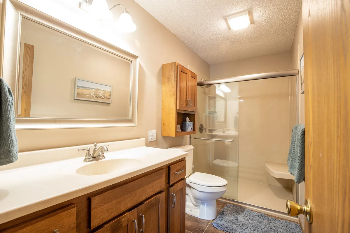 A modern bathroom featuring a vanity with sink, framed mirror, shower area, and wooden cabinet. The setting is fresh, tidy, and inviting, ideal for moments of self-care and relaxation.