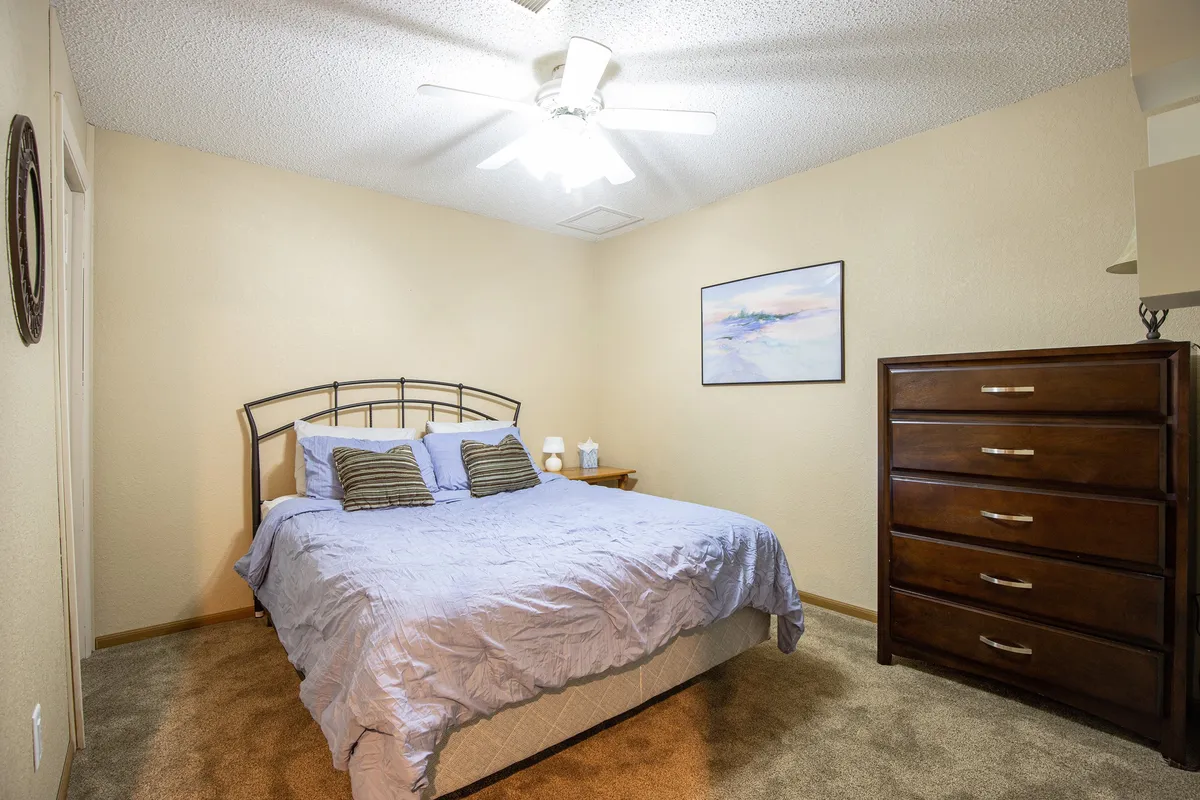 A serene bedroom with a comfortable bed, a dresser, and artwork adorning the walls. The space is bathed in soft sunlight, evoking feelings of relaxation and restful sleep.
