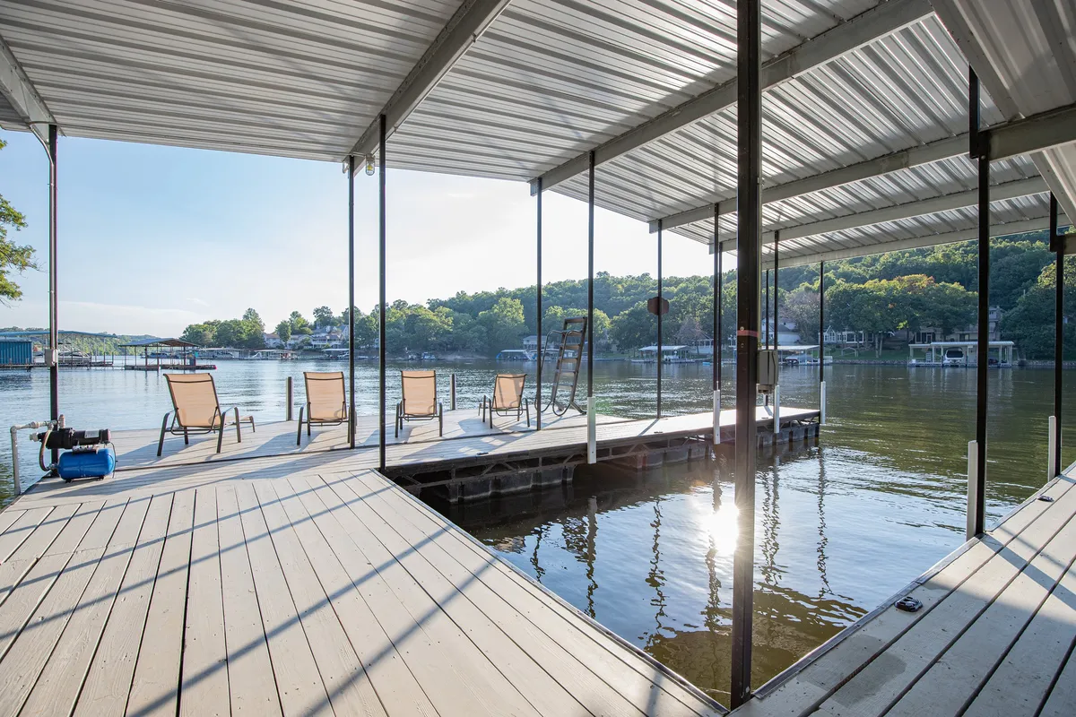 A relaxing lakeside scene featuring lounge chairs on the dock overlooking the water, with surrounding trees providing a sense of privacy and intimacy. The image evokes leisure and outdoor enjoyment, and the dock clearly supports both fishing and boating activities.