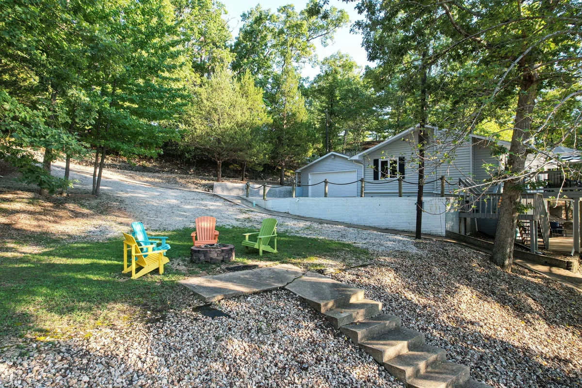 A cheerful firepit area surrounded by colorful chairs, situated among trees and connected by a gravel path. The setting is ideal for evening gatherings, storytelling, and stargazing, with the house in the background suggesting convenient access to indoor comforts.