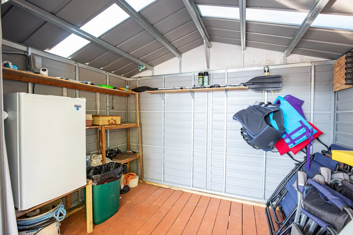 Inside a practical storage shed, this image shows a refrigerator, life jackets, and fishing gear organized on shelves. It directly references the dockside shed equipped for anglers, highlighting the amenities that support fishing and boating outings.
