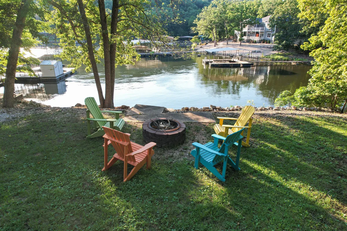 A cozy lakeside firepit area with colorful Adirondack chairs arranged for group gatherings, offering a beautiful view of the water and lush greenery all around. The scene evokes warmth and relaxation, ideal for evening socializing.